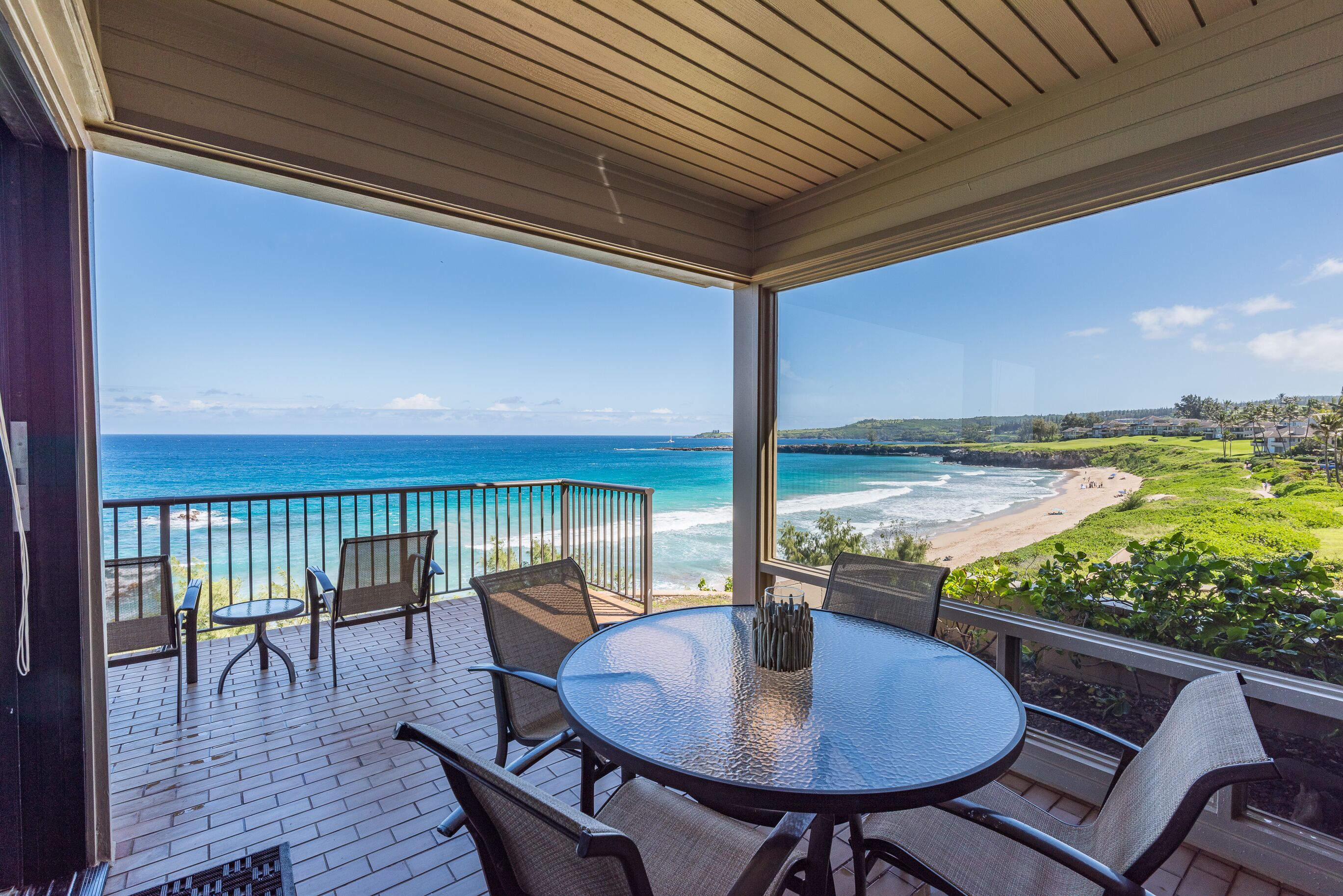 A covered outdoor patio with a round table and chairs, overlooking a beach and ocean.