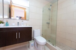 Et moderne badeværelse med en glasbrusekabine, et hvidt toilet og en mørk trækommode med et spejl over.
