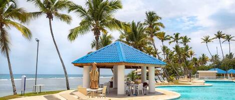 A beachside resort with a pool, lounge chairs, and a gazebo.