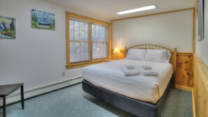 Une chambre à coucher bien rangée, avec un lit, une fenêtre équipée de stores, une lampe et deux tableaux accrochés au mur.