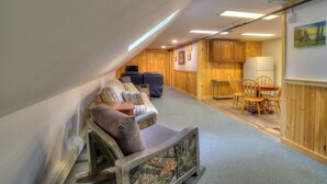 Une pièce chaleureuse avec un plafond en pente, des murs en bois, un coin repas avec une table et des chaises, un canapé agrémenté de coussins à motifs et une petite table avec une lampe.