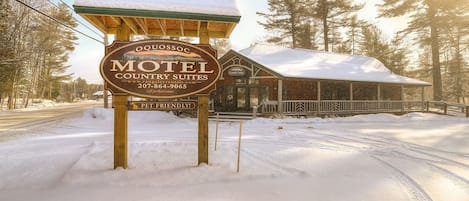 A snow-covered motel sign with a wooden structure, surrounded by trees and a clear sky.