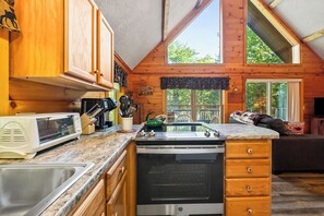 A cabin interior with a kitchen, dining area, and a large window offering a view of the outdoors.