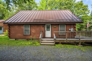 A small, single-story log cabin with a metal roof, a front porch, and a flagpole. - Lupine Lodge - Adorable, newly renovated cottage, with water access and dock on Loon Lake (Rangeley)