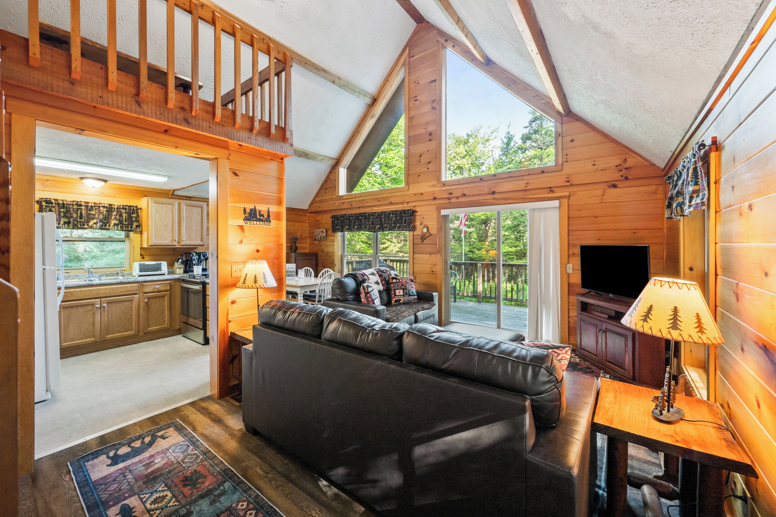 A cozy cabin interior with a living room, kitchen, and a balcony with a view of the outdoors.