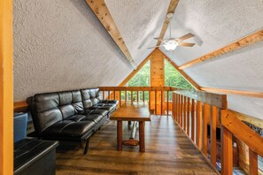 Une pièce mansardée chaleureuse avec un plafond en bois, un canapé en cuir noir, une table en bois et une vue sur l’extérieur.