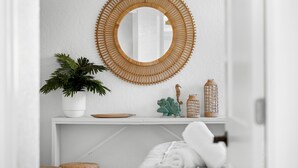 A white room with a round mirror, a potted plant, and decorative items on a shelf. - Plumeria Villa by Beach Boutique Rentals (Holmes Beach)