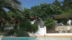 A pool area with a clear blue pool, surrounded by lush greenery and a stone wall. - Paradise Found - A Greek Retreat With The View (Skopelos)