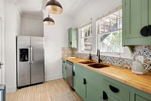 A kitchen with a stainless steel refrigerator, a sink, and a window with a view of greenery outside. - Blithely Baroque (Atlanta)