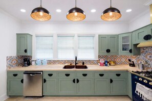 A kitchen with green cabinets, a double sink, a dishwasher, and a stove. - Blithely Baroque (Atlanta)