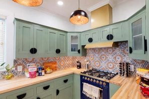 A kitchen with teal cabinets, a patterned backsplash, a wooden countertop, and a blue stove. - Blithely Baroque (Atlanta)