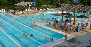 Ein Schwimmbecken mit mehreren Bahnen, Liegestühlen, Sonnenschirmen und einer überdachten Sitzgelegenheit.