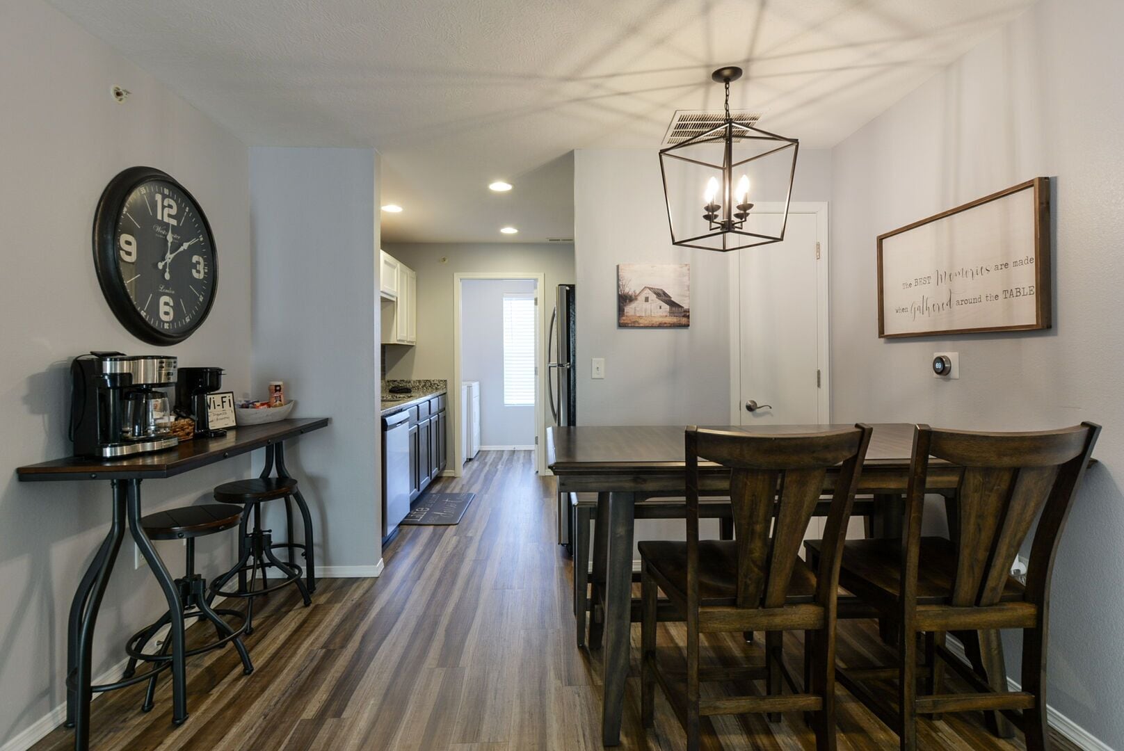 Une cuisine moderne équipée d’une machine à café, d’une horloge et d’un coin repas avec des chaises et une table en bois.