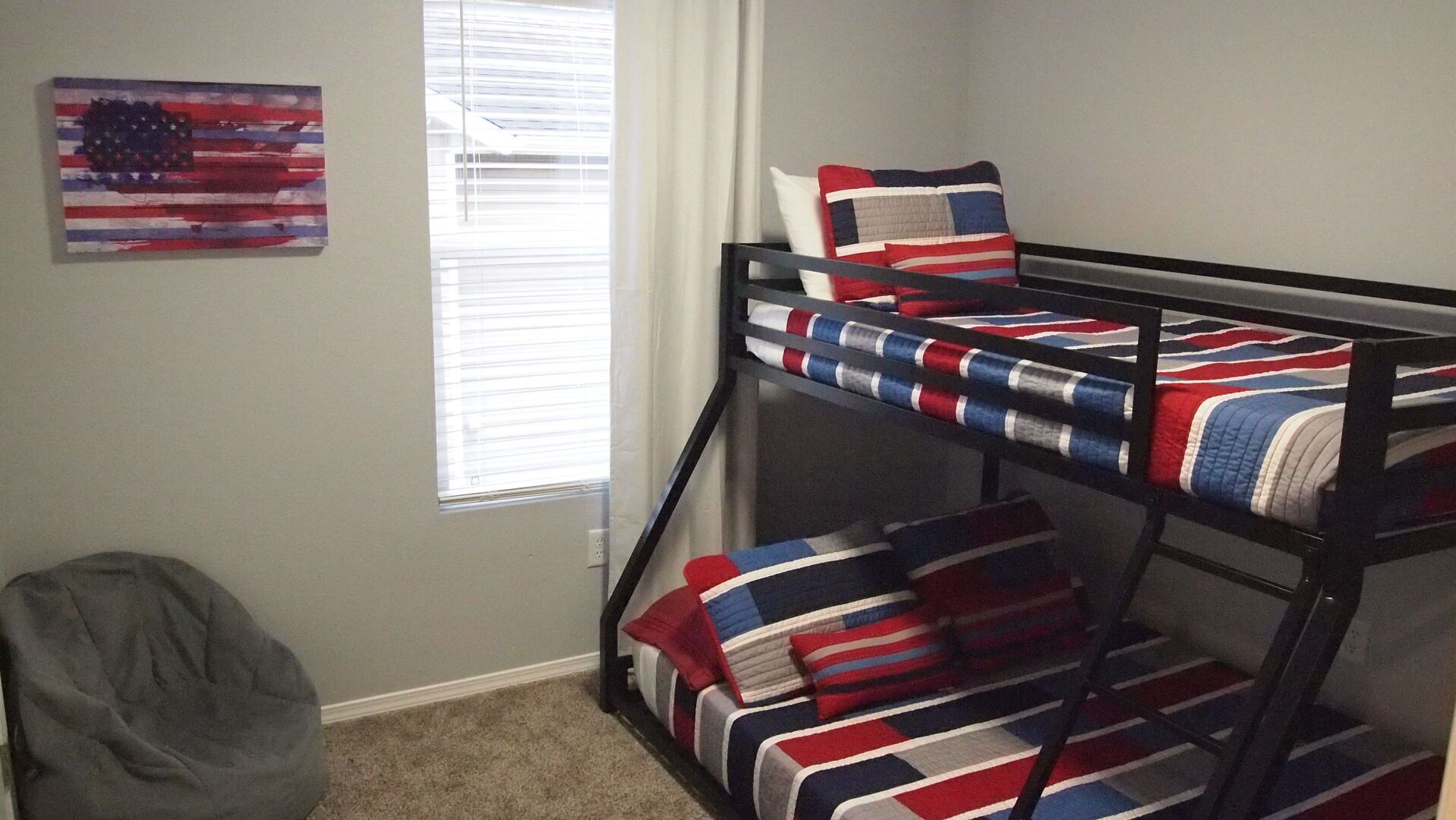 A bunk bed with a British flag design, a gray bean bag chair, and an American flag painting on the wall.
