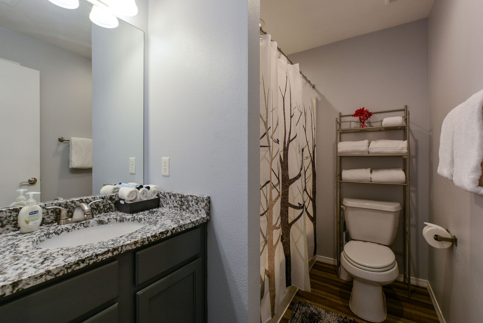 Une salle de bain avec un comptoir en granit, des toilettes, un rideau de douche orné d’un motif d’arbre et un porte-serviettes.