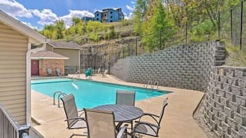 Une piscine bordée d’un mur en pierre, avec en arrière-plan un bâtiment bleu.