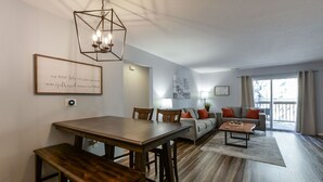 Un soggiorno moderno con zona pranzo, caratterizzato da un tavolo in legno, divani e un lampadario.