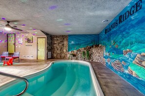 Piscina interna com um mural intitulado "Island's Ridge", paredes de pedra e um ventilador de teto.