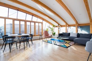 Amplia sala de estar con techo alto, vigas de madera, una mesa redonda de comedor con sillas, un sofá y una mesa de centro.