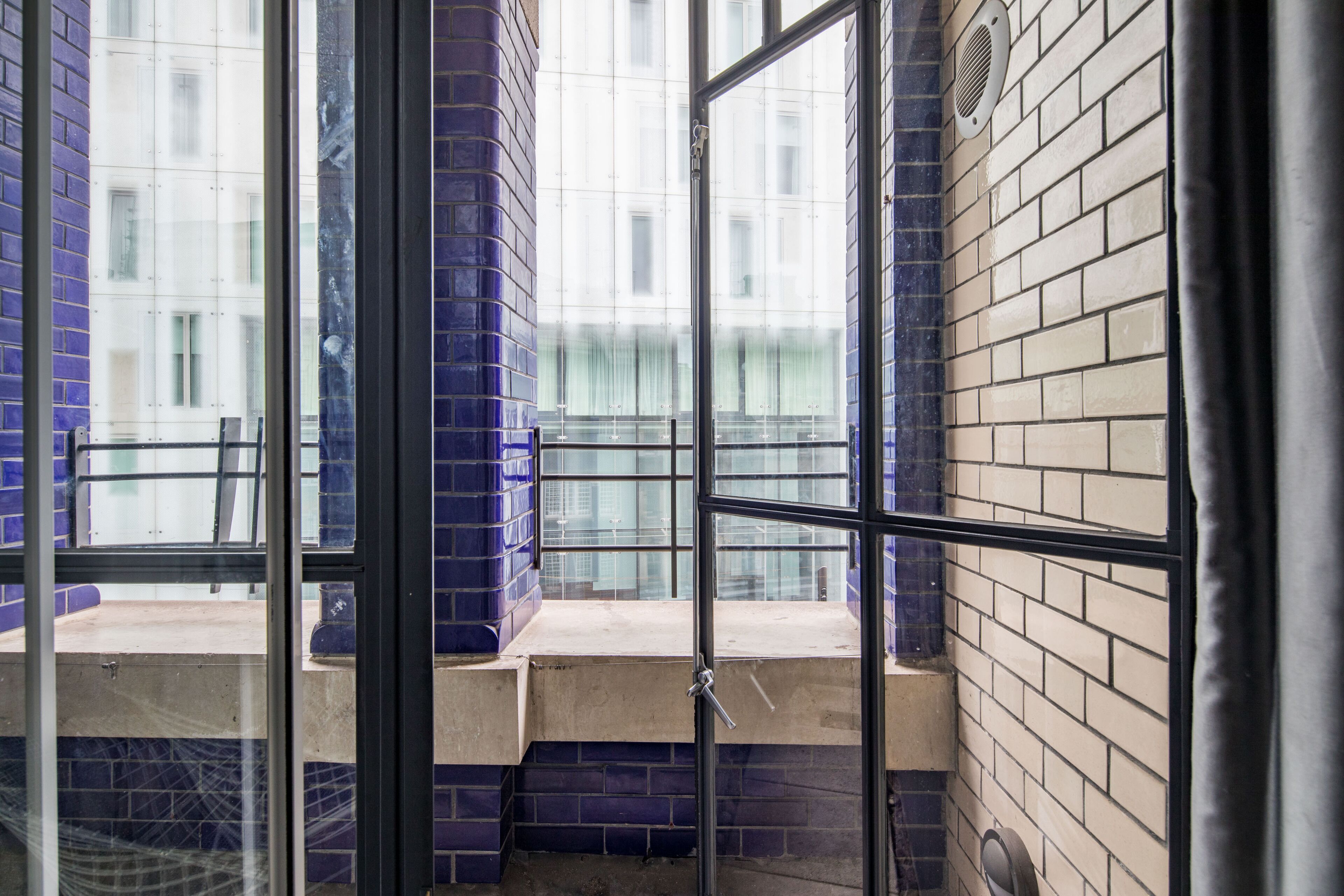 A room with a large window, a tiled wall, and a metal railing.