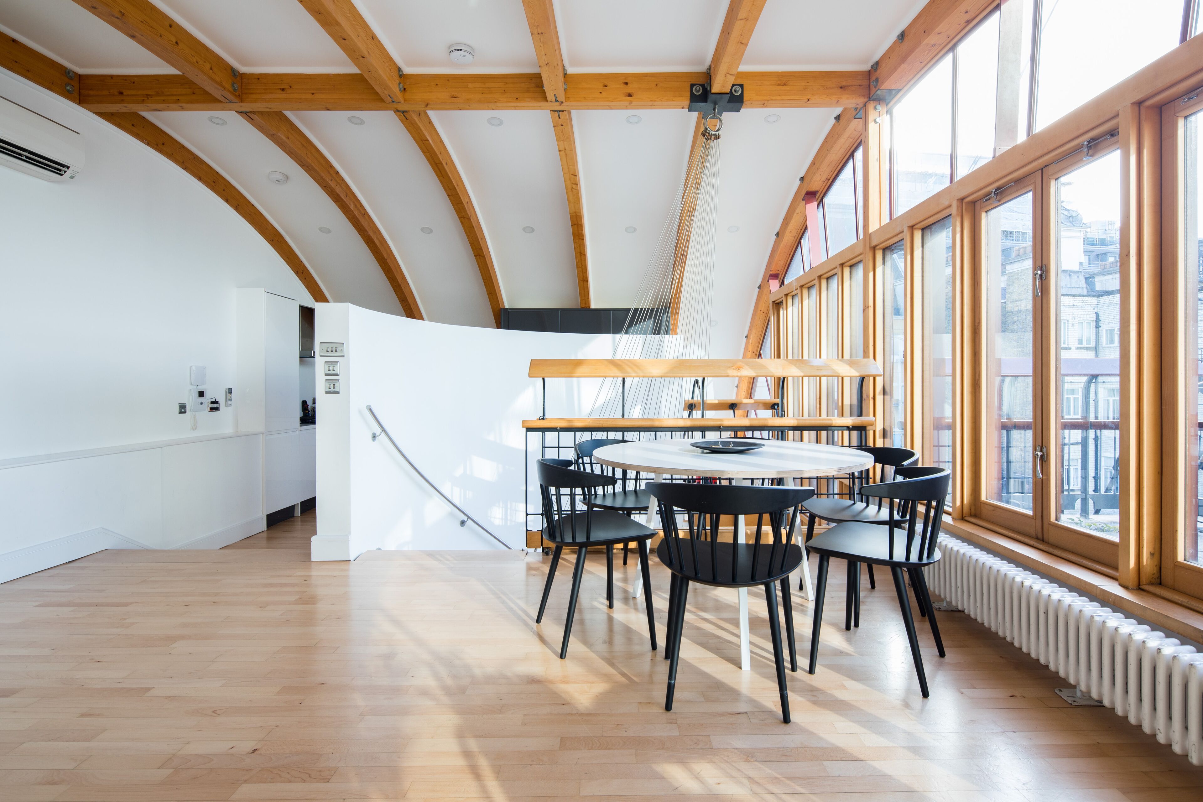 A spacious room with a wooden ceiling, a round table with chairs, and large windows.