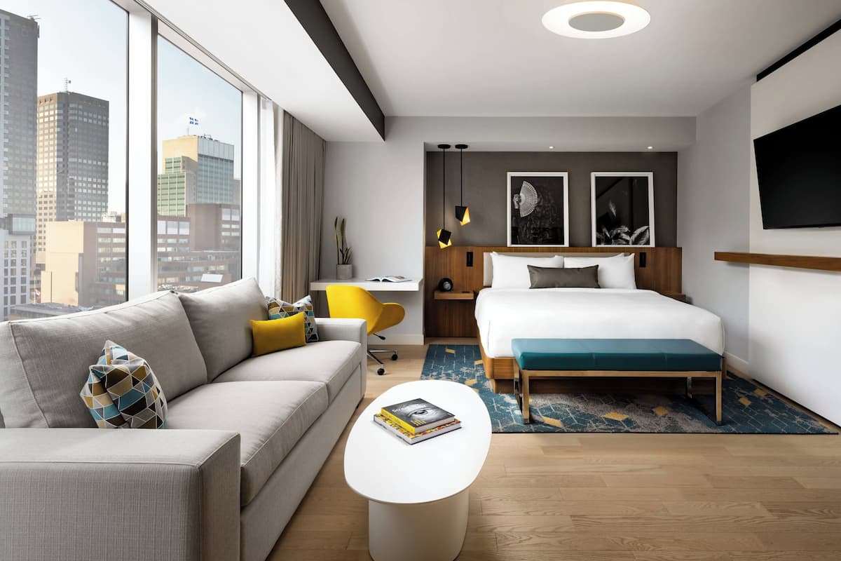 A modern hotel room with a large bed, a sofa, a desk, and a TV.