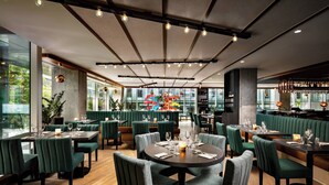 A modern restaurant with green upholstered booths, wooden tables, and a central decorative light fixture. - Humaniti Hotel Montreal, Autograph Collection (Montreal)