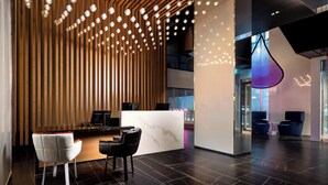 A modern reception area with a wooden slatted wall, a marble reception desk, and black leather chairs. - Humaniti Hotel Montreal, Autograph Collection (Montreal)