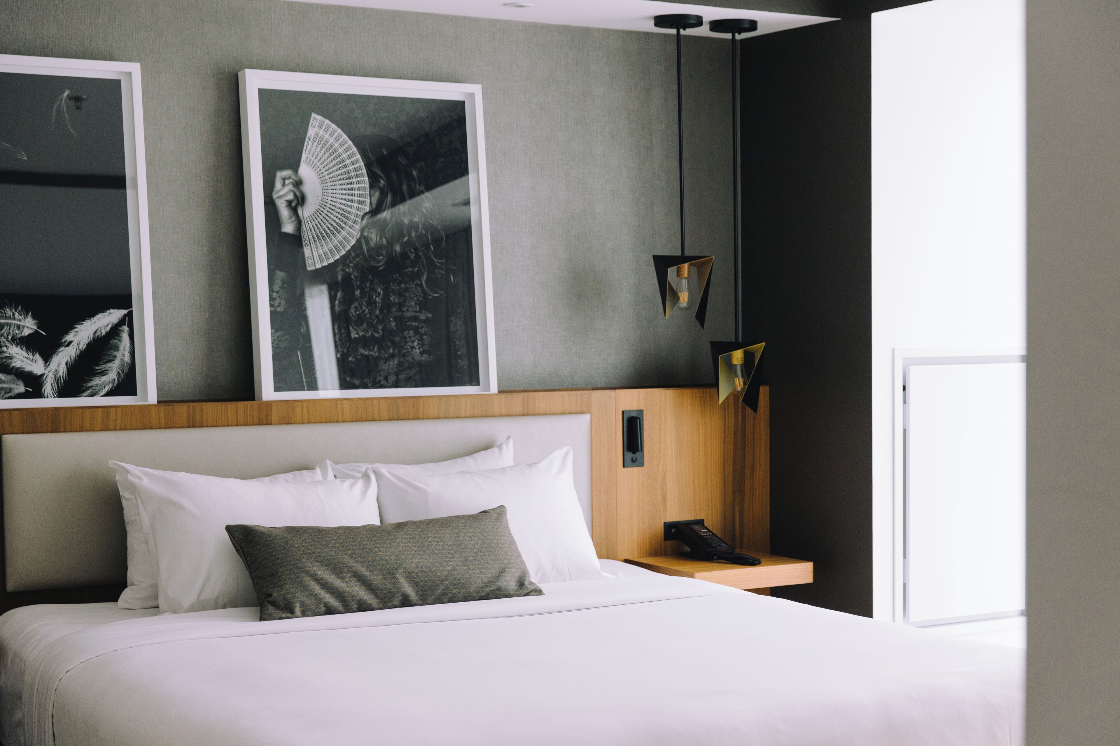 Hotellihuone, jossa on suuri sänky, puinen pääty, yöpöytä, jossa on puhelin, ja kaksi kehystettyä kuvaa seinällä.