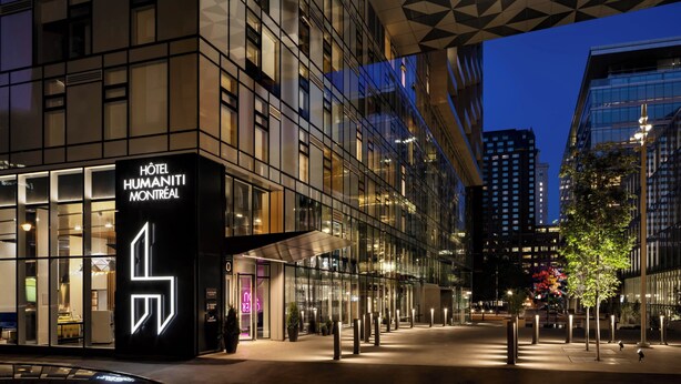 A modern hotel with a prominent geometric logo, large glass windows, and a well-lit entrance area. - Humaniti Hotel Montreal, Autograph Collection (Montreal)