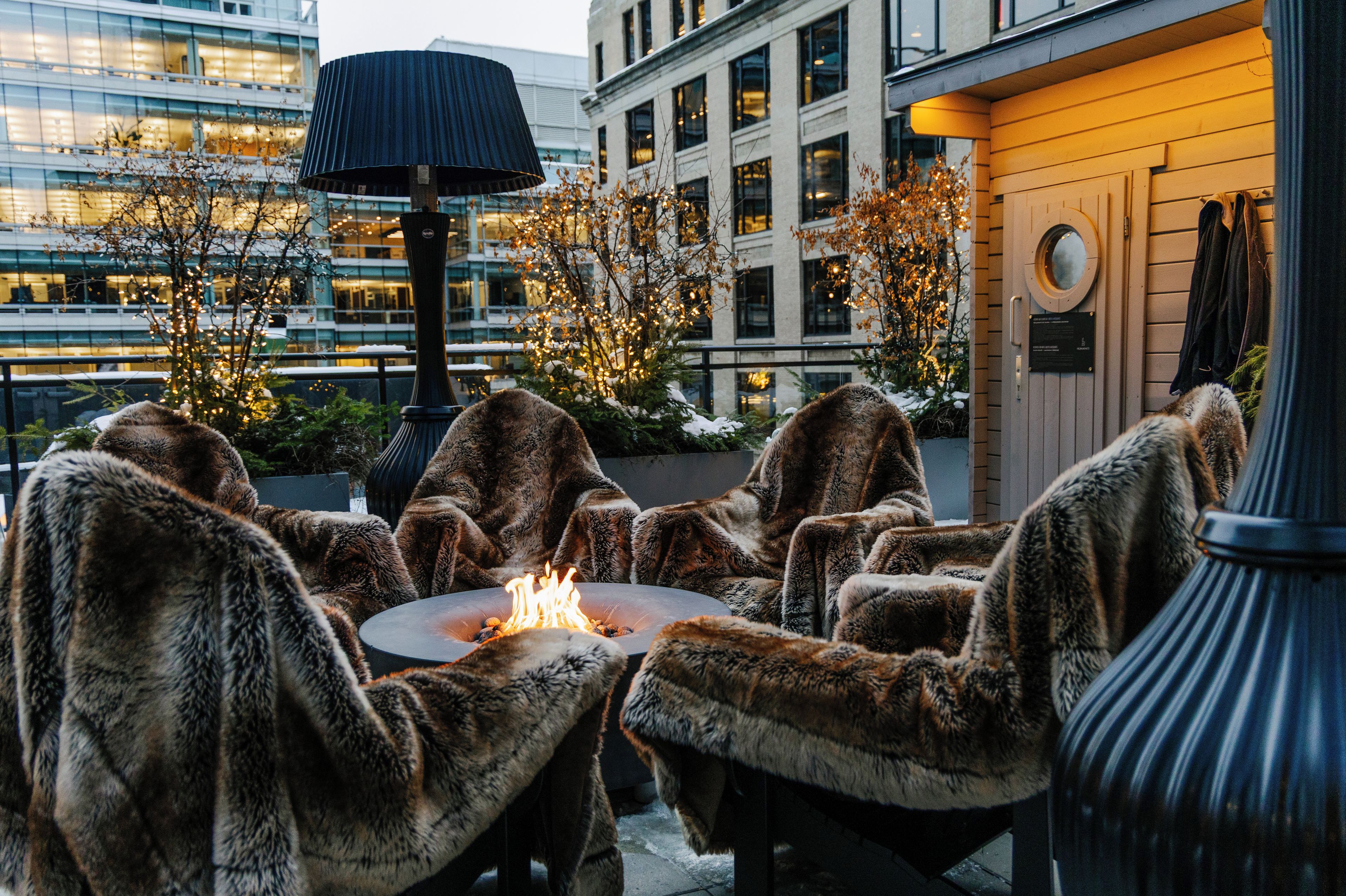 Outdoor seating with fur chairs and a central fire feature.
