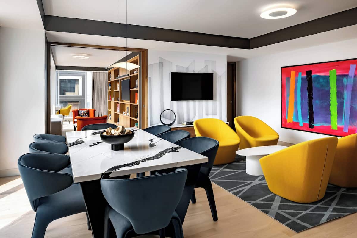 A modern living room with a dining area, a flat-screen TV mounted on the wall, and a colorful abstract painting.