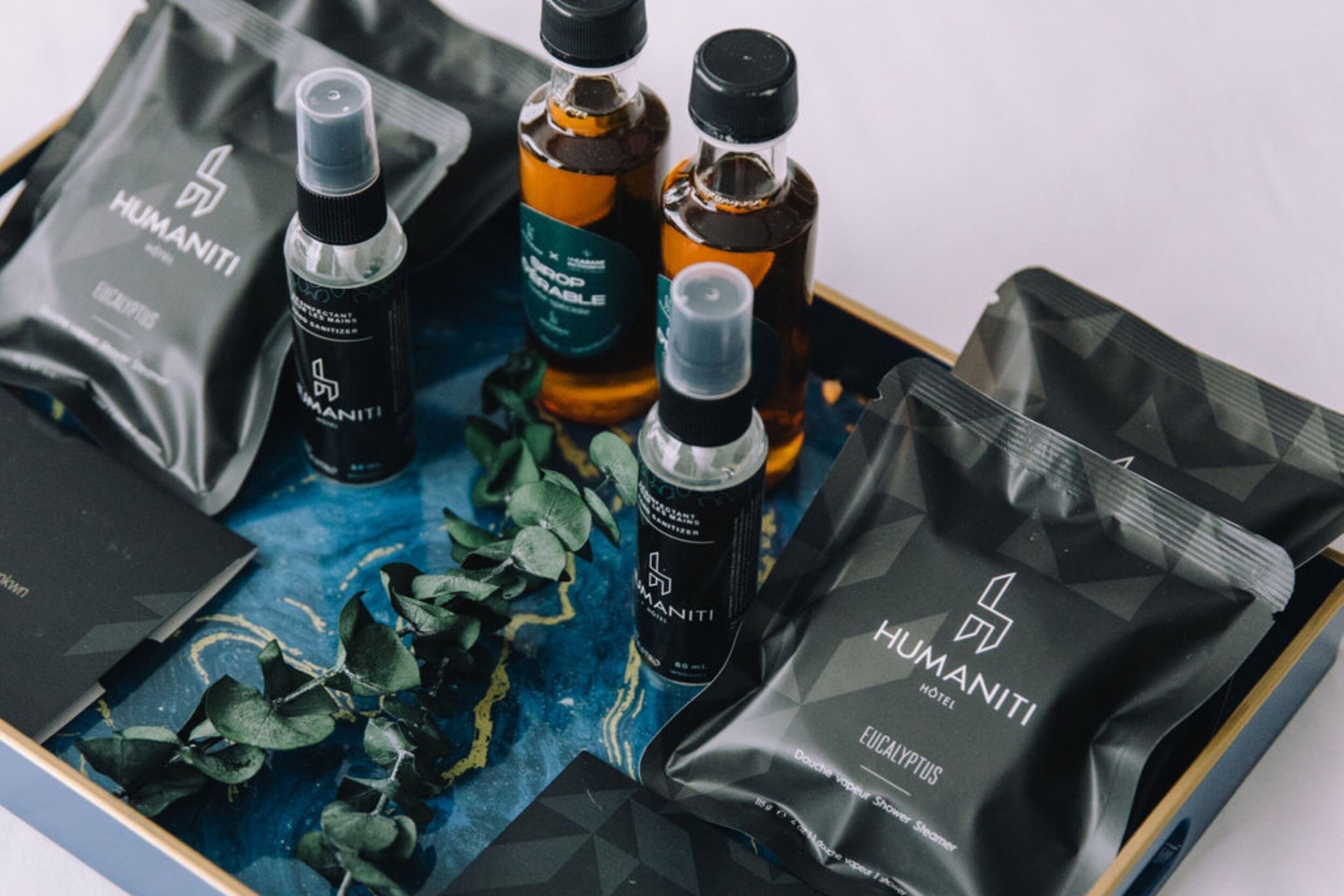 Un juego de bolsas negras con el logo 'HUMANITI', una botella de líquido y una caja negra sobre una superficie estampada en azul.