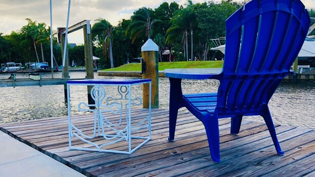 A wooden deck with a blue chair and a white metal table. - Cozy Florida Waterfront Home (Sarasota)