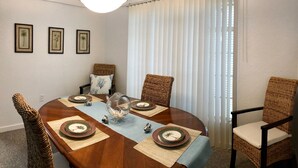 A dining room with a round table set for four, surrounded by wicker chairs with cushions. - Cozy Florida Waterfront Home (Sarasota)
