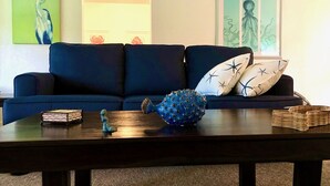 A dark blue sofa with star-patterned pillows, a wooden coffee table with decorative items, and wall art including a bird and a human figure. - Cozy Florida Waterfront Home (Sarasota)