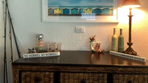 A wooden cabinet with a framed picture of colorful beach houses, a lamp, and a sign that reads "NO HURRIES, NO WORRIES". - Cozy Florida Waterfront Home (Sarasota)