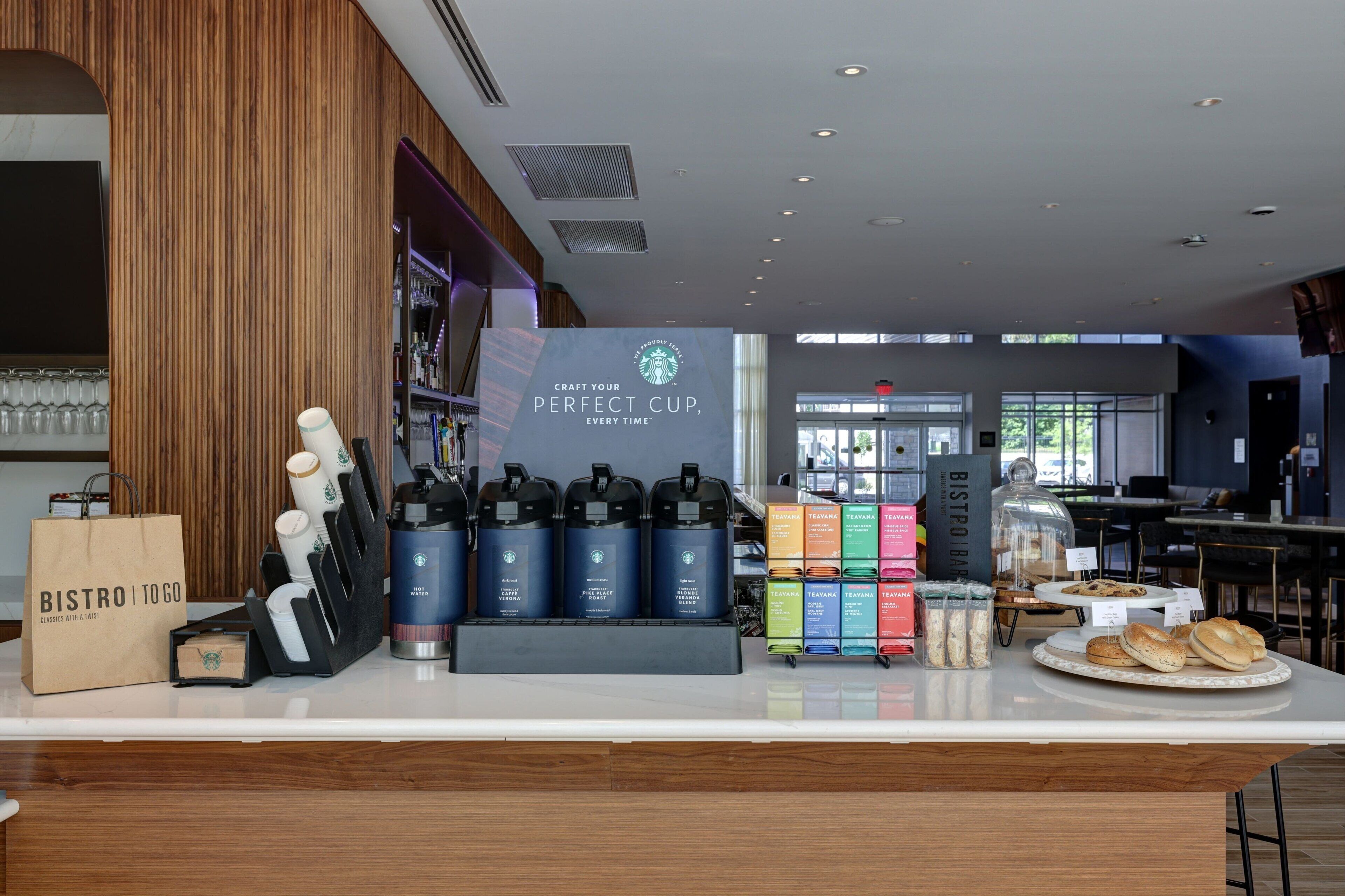A Starbucks coffee shop interior with a coffee machine, tea dispensers, and pastries on display.