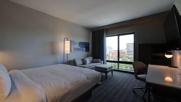 A hotel room with a large bed, a sofa, a desk, and a TV.