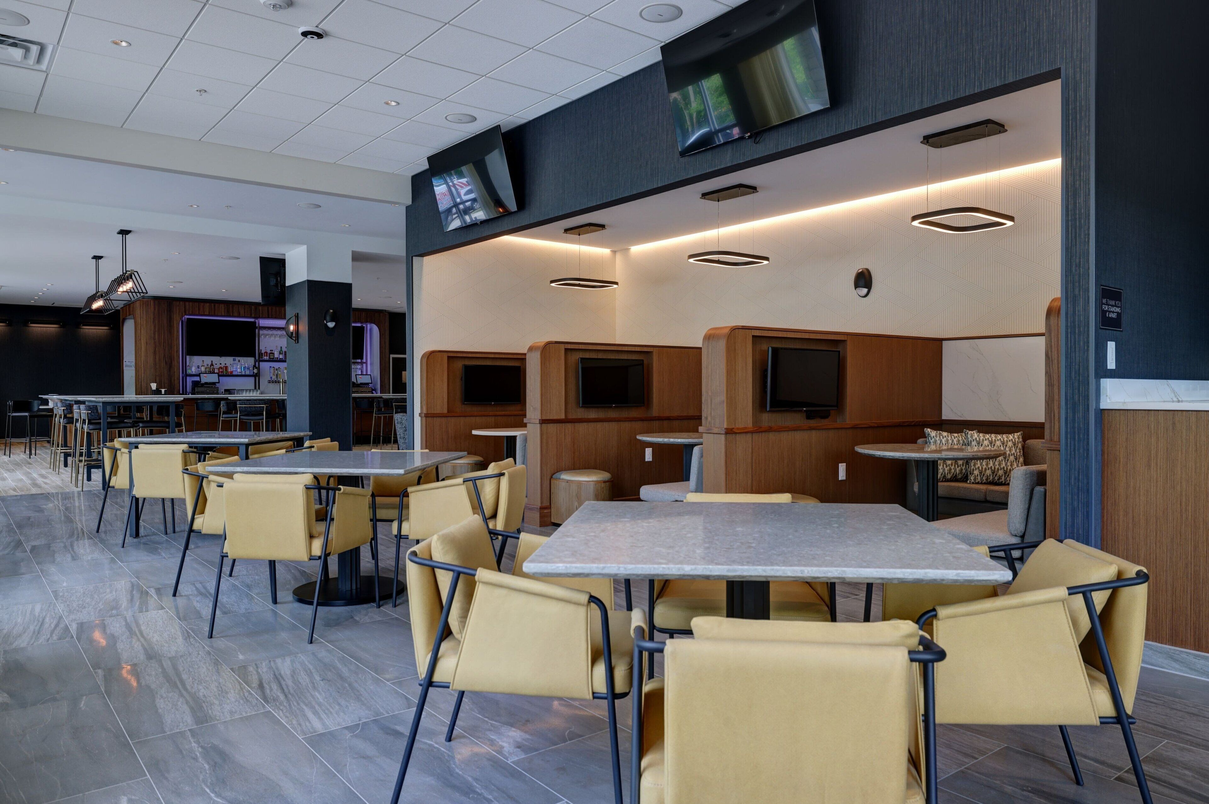 A modern restaurant with multiple seating areas, including tables and booths, and a bar in the background.