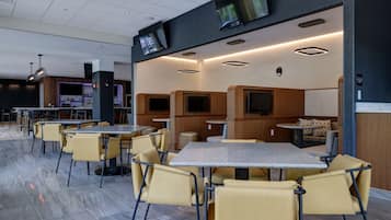 A modern restaurant with multiple seating areas, including tables and booths, and a bar in the background.