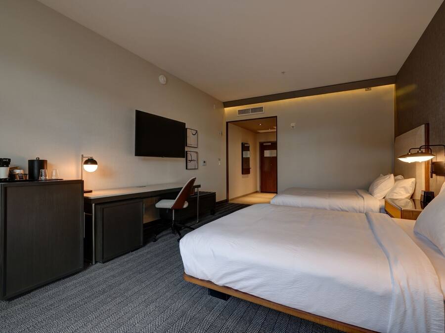 A hotel room with a bed, a desk, a chair, a television, and a lamp.