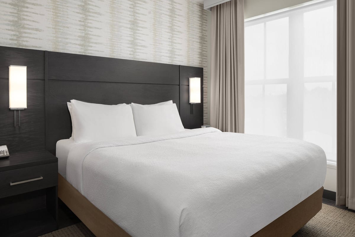 Una habitación de hotel con una cama grande, dos mesitas de noche y una mesita auxiliar con teléfono.