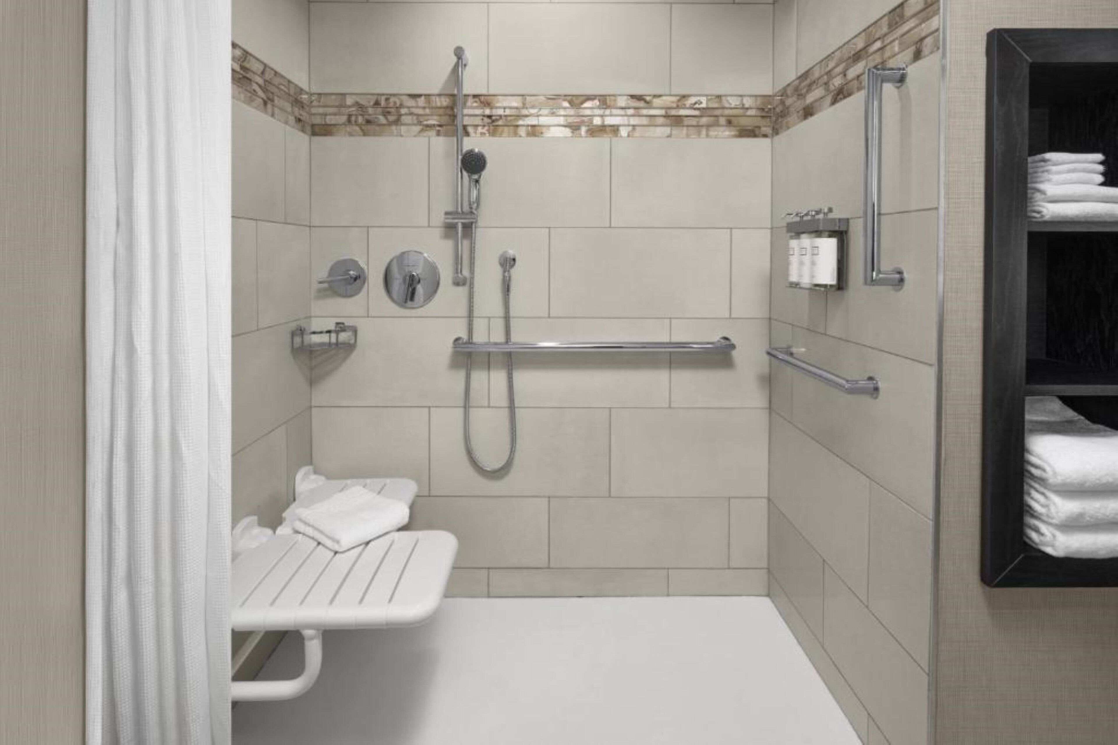 A modern bathroom with a shower, grab bars, a bench, and a towel rack.