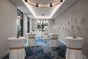 Un couloir d’hôtel avec des tables rondes, une moquette à motifs et des œuvres d’art décoratives accrochées aux murs.