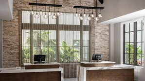 Un área de recepción con pared de ladrillo, ventanas amplias con cortinas translúcidas y una moderna disposición de escritorio.
