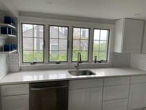 A kitchen with white cabinets, a stainless steel sink, and a window overlooking a brick building.