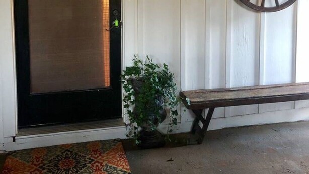 Une porte d’entrée avec un cadre noir, un luminaire fixé au mur, une roue décorative et un banc.