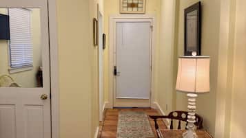 A hallway with a closed door, a table with a lamp, and a bed with a white bedspread.