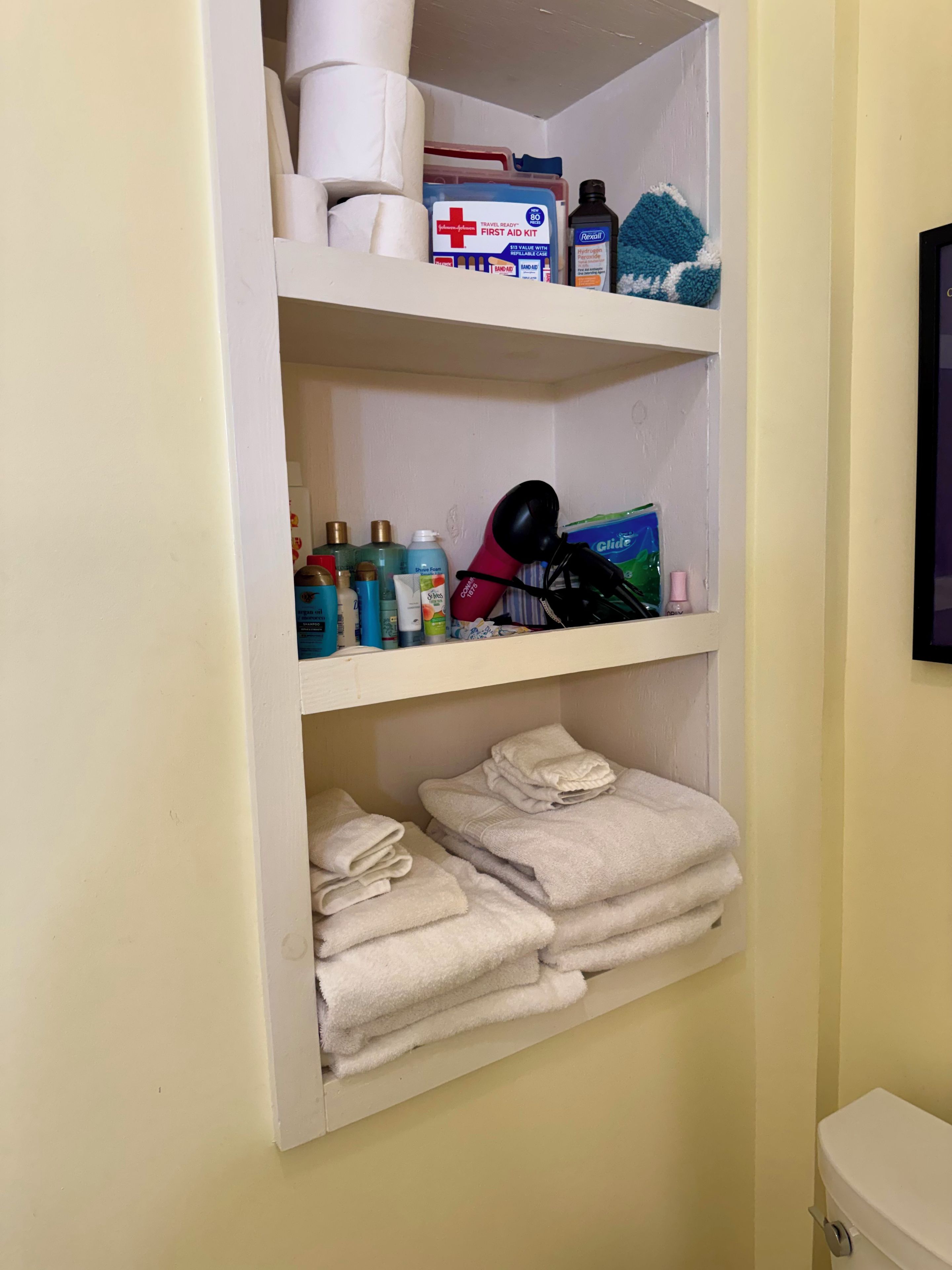 A storage shelf with toiletries, a first aid kit, and folded towels.